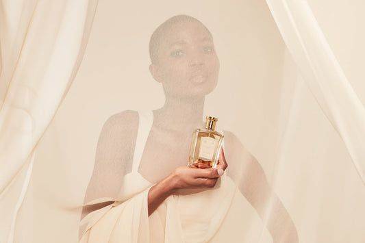 A bottle of Bouquet de la Reine, behing held by a woman behing a sheer piece of fabric. 