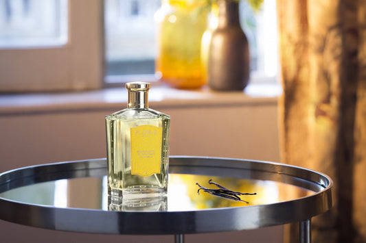 A Bottle of Bergamotto di Positano Eau de Parfum from Floris London upon a mirrored table with a few pods of vanilla next to it. 