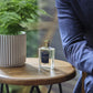 A 71/72 - Eau de Parfum by Floris London rests on a wooden table near a potted plant and someone in a blue jacket.