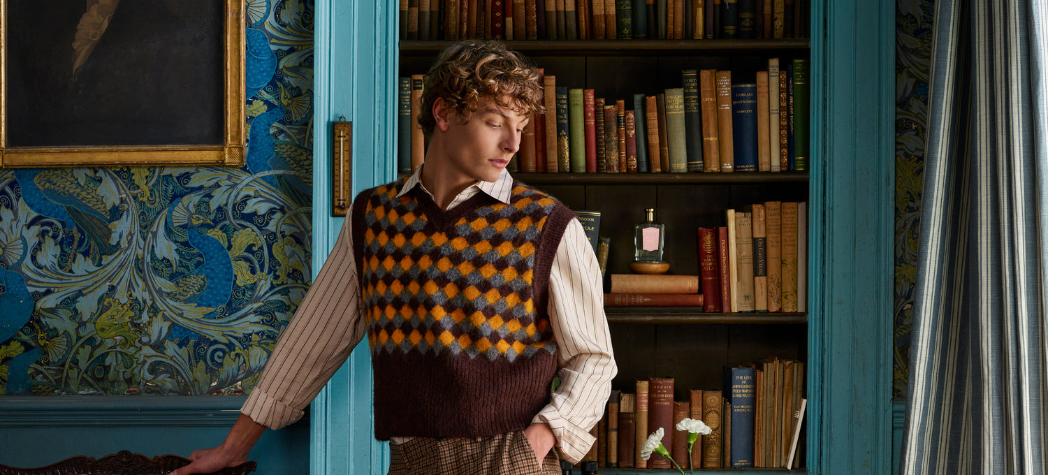 A man stands in front of a bookcase, with a bottle of Floris London Malmaison Encore placed on a shelf