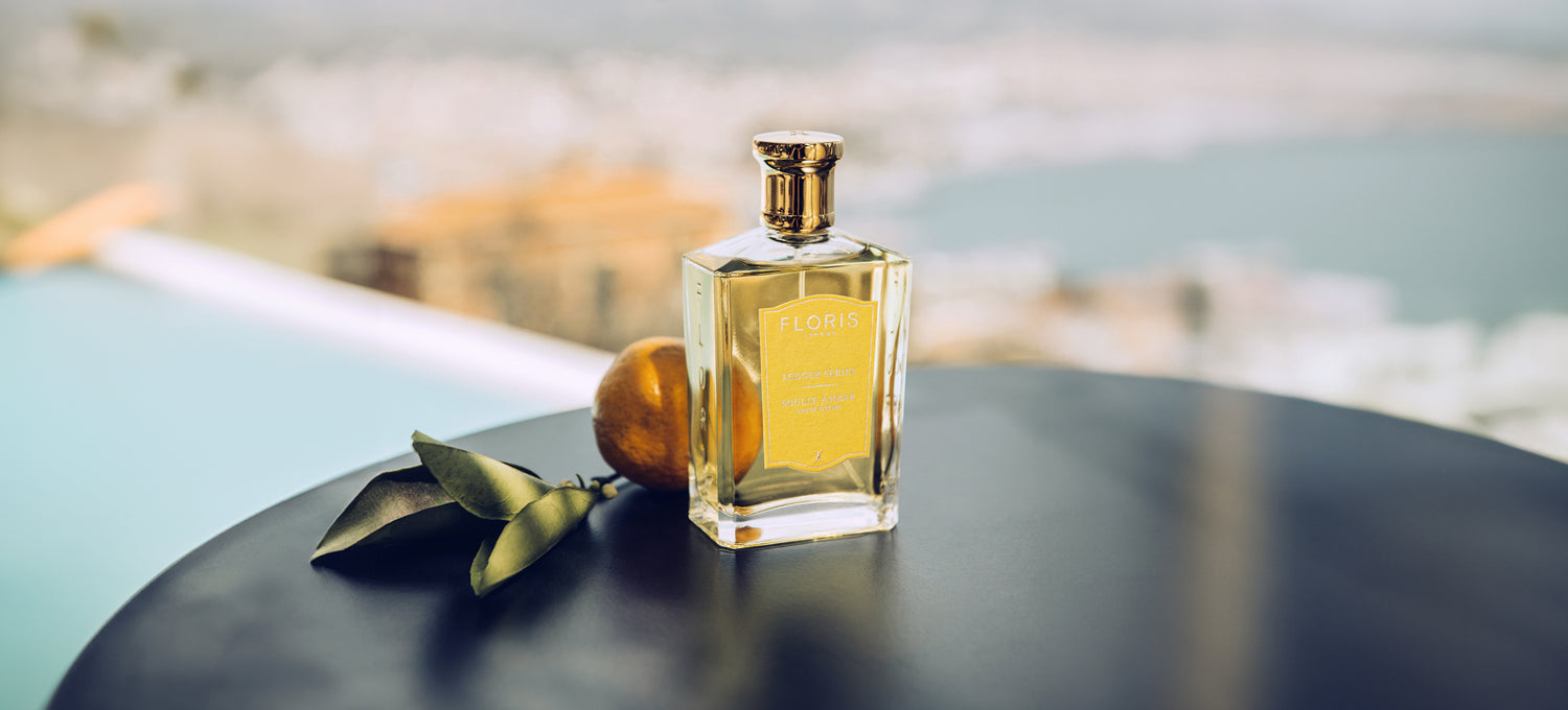 On the shores of Spain a bottle of Floris London Soulle Ambar its on a black table with an orange.