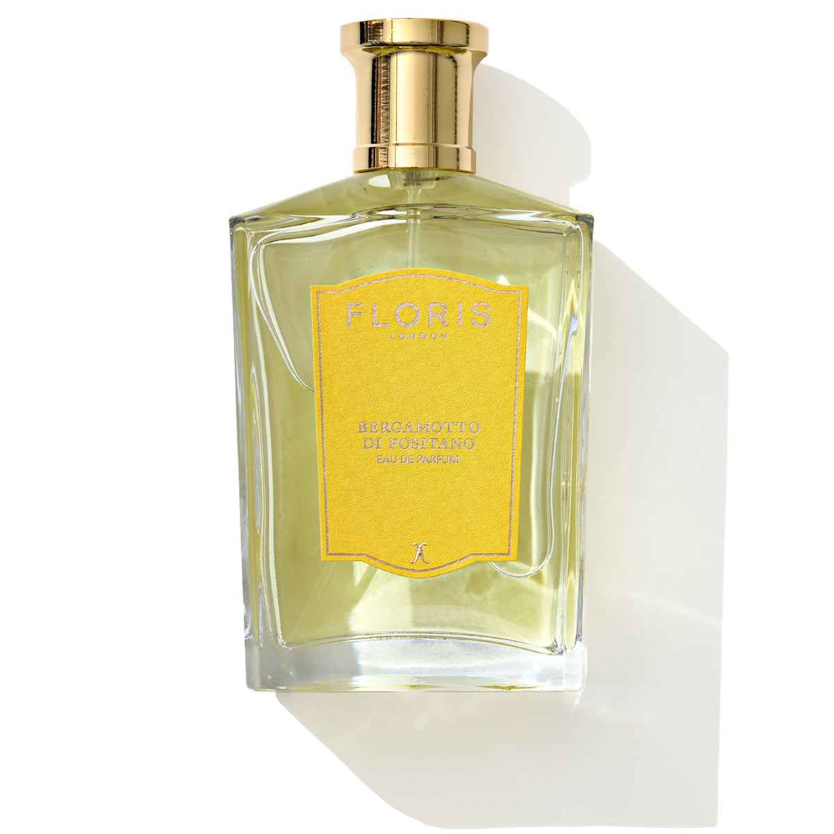 A bottle of Floris London Bergamotto di Positano - Eau de Parfum, adorned with a yellow label and a gold cap, exudes marine notes as it casts a shadow.