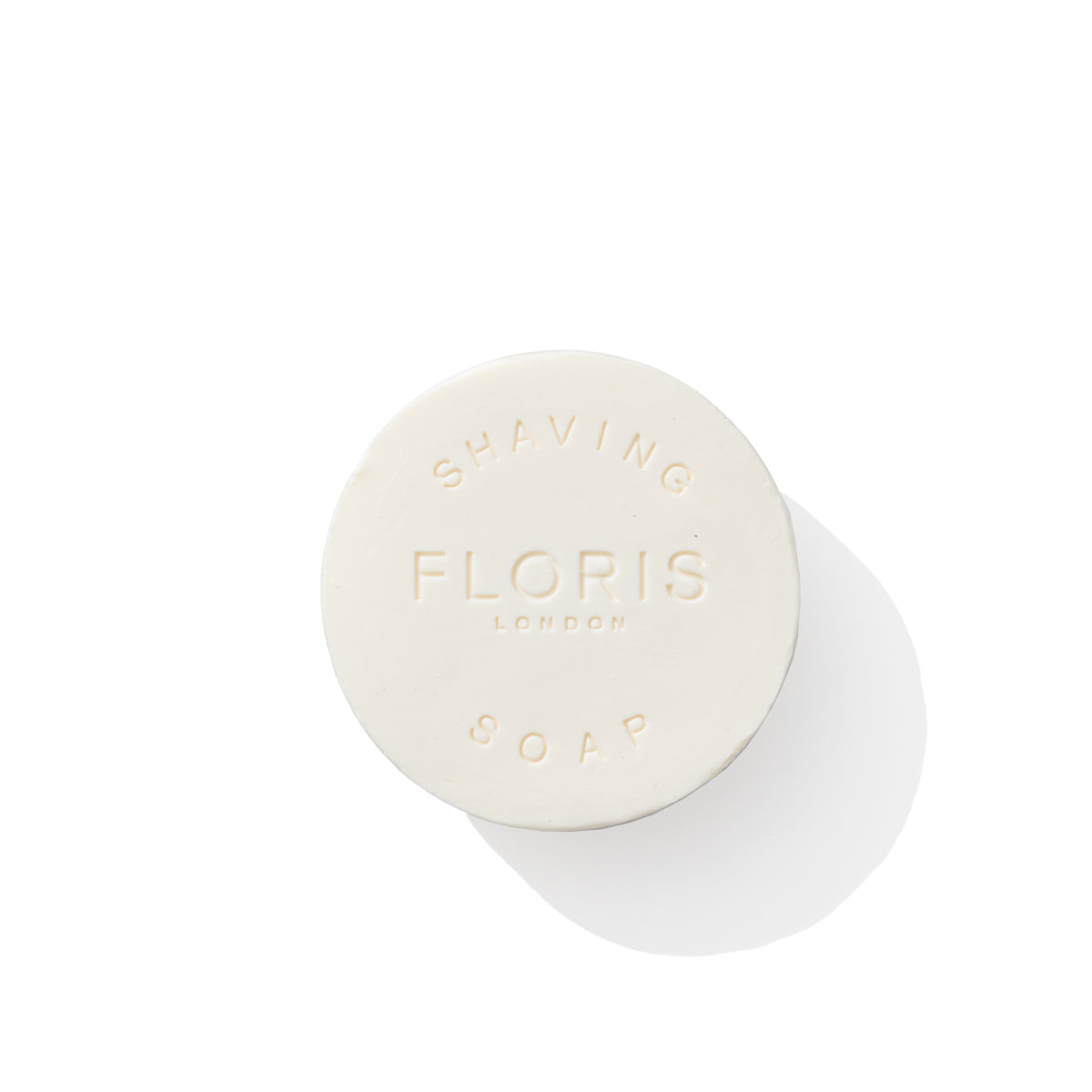 The Elite Shaving Bowl Refill 100g from Floris London displays an elegant round design with embossed text on a white background, exuding subtle woody notes. Enriched with shea butter, this luxurious soap ensures a smooth and nourishing shave.