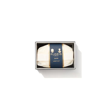 Floris London's Elite Soap 100g has a dark blue and gold label, emits woody notes with a citrus twist, and is viewed from above on a white background.