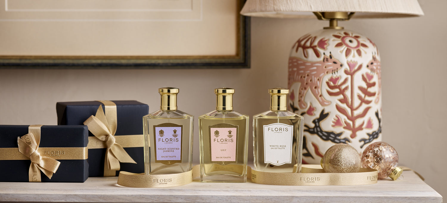 Floris London Fragrances for her includeing Night Scented Jasmine, Lily and White Rose, placed upon a dressing table surrounded by ribbon and gift wrapped products. 