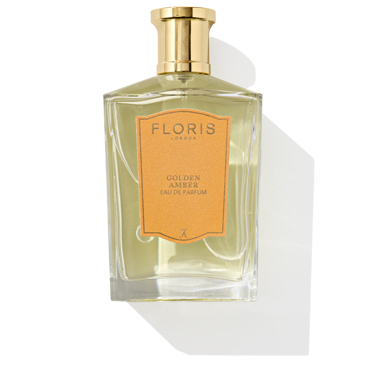 A clear glass bottle of Floris London's Golden Amber - Eau de Parfum, featuring a gold cap and an orange label, is elegantly displayed against a white background, highlighting its refined vegan fragrance.