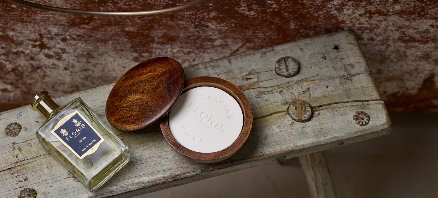 A bottle of Floris No. 89 Eau de Toilette, next to the Shaving Soap & Bowl. Placed upon a wooden milking stool, besides a vintage bathtub. 