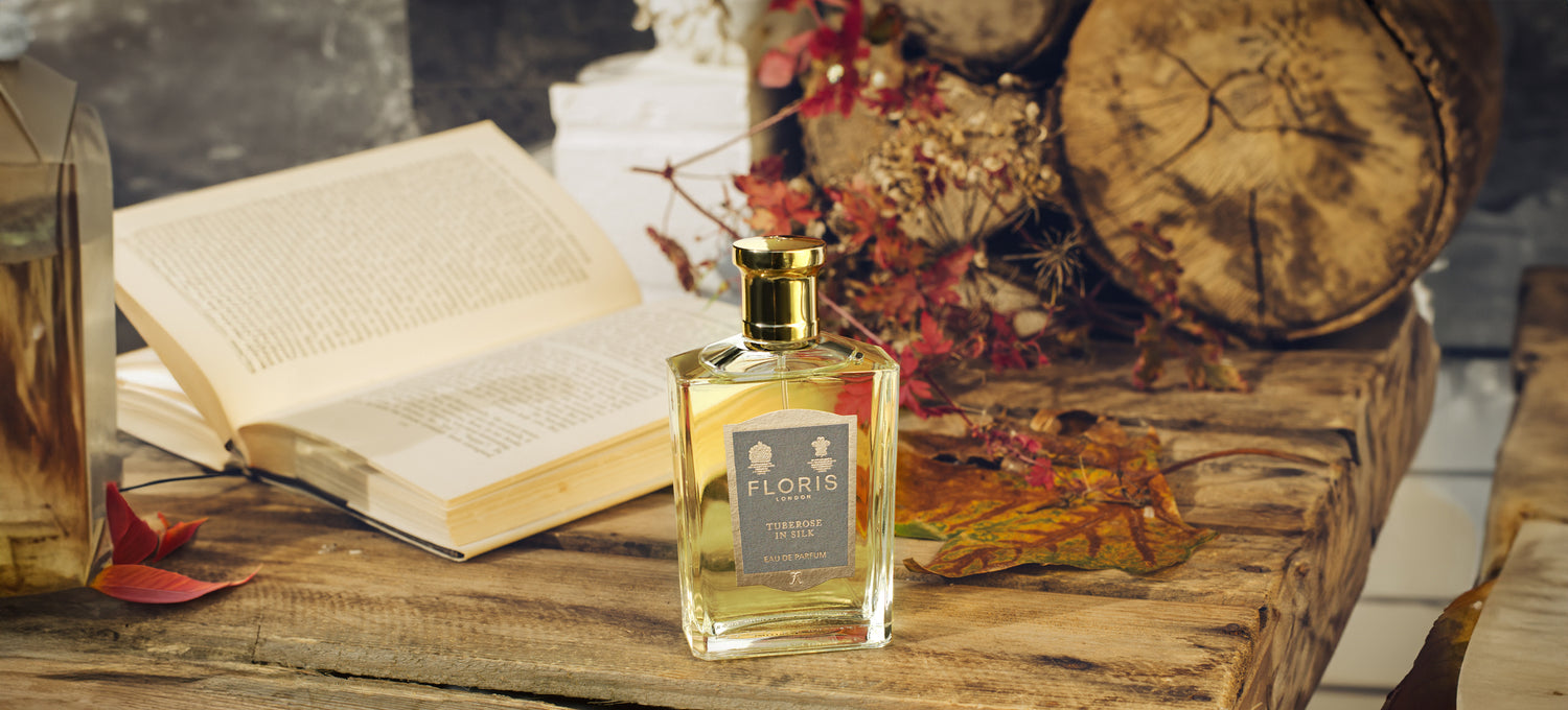 A Bottle of 'Tuberose in Silk', upon a wooden table with a open book and autumn foliage. 