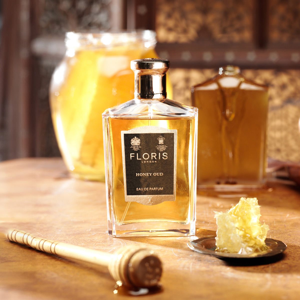 A cozy setting with a Floris London Honey Oud Eau de Parfum bottle, English honeycomb, a honey dipper, and touches of oud oil.