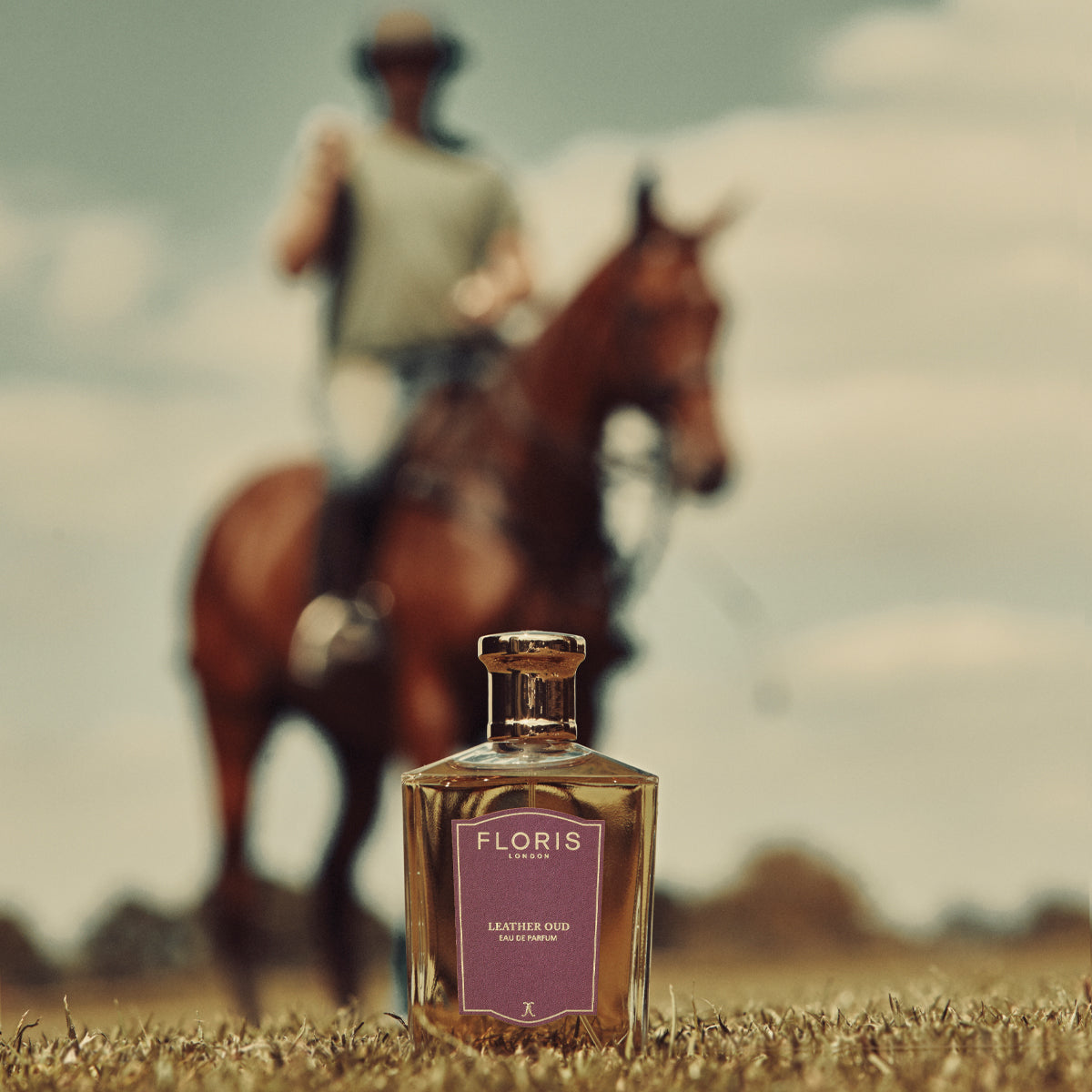 Leather Oud Eau de Parfum by Floris London in focus, with a horseback rider blurred in the background under a clear sky.