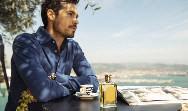 A man sat with a cup to tea on the shores of Spain in the background with a bottle of Floris London Soulle Ambar