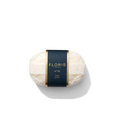 A bar of finely milled No. 89 Soap by Floris London, wrapped in white paper and adorned with a black label featuring gold accents, set against a white background.