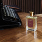 A "Santal" perfume bottle by Floris London is on a wooden desk next to a vintage typewriter, emitting a rich, woody fragrance ideal for men.