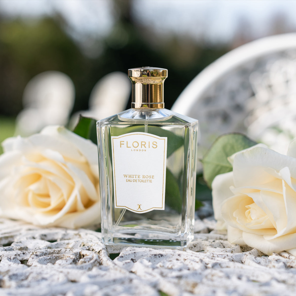 Floris London's White Rose - Eau de Toilette bottle is nestled among velvet roses and warm amber tones on a textured surface.